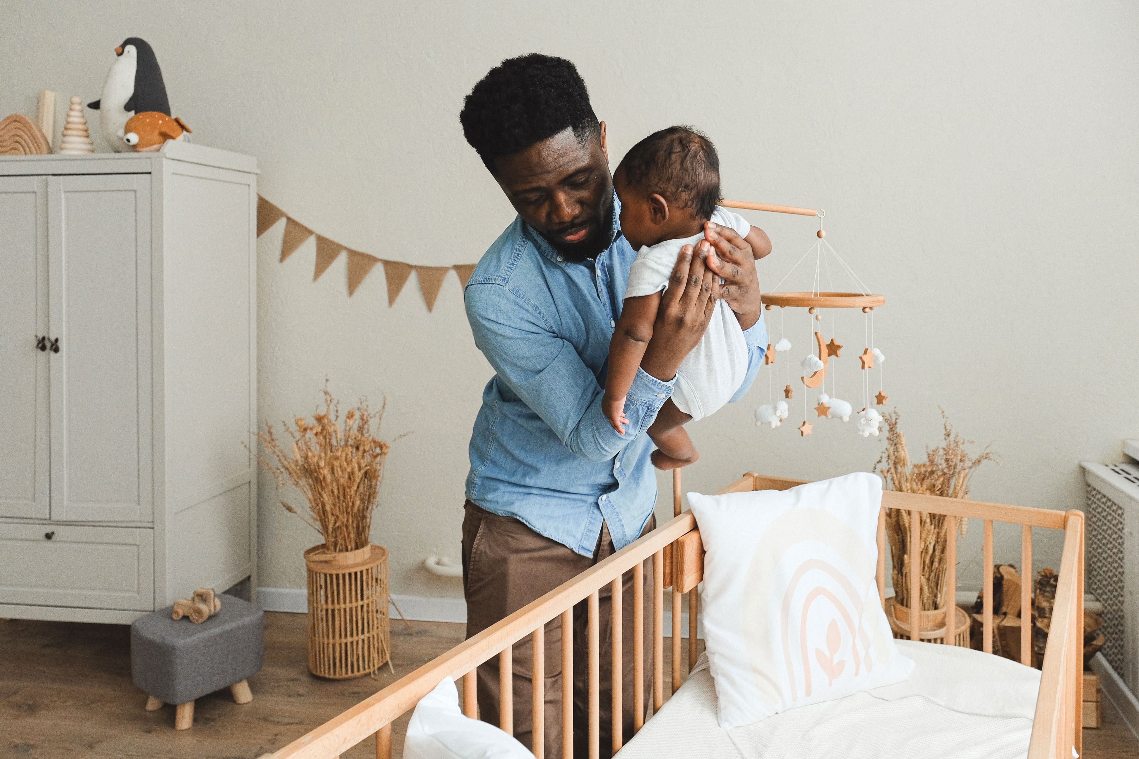 Father gently placing his baby into a wooden nursery crib — BabyCosts Australia